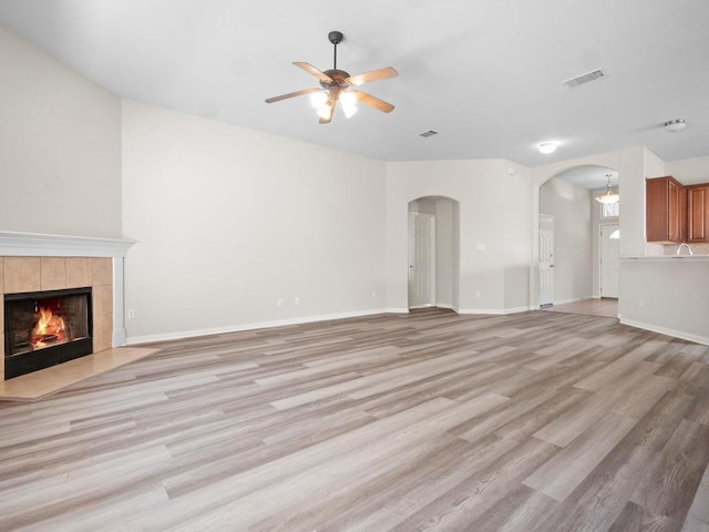 429 Falcon Ln, Leander, TX 78641 - unfurnished living room with a ceiling fan, arched walkways, light wood finished floors, and a tiled fireplace