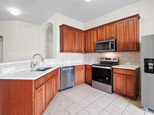 429 Falcon Ln, Leander, TX 78641 - kitchen with appliances with stainless steel finishes, decorative backsplash, a peninsula, brown cabinetry, and light countertops