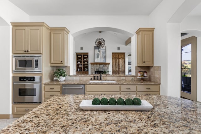 219 Jack Nicklaus Dr, Austin, TX 78738 - kitchen with appliances with stainless steel finishes, cream cabinetry, decorative backsplash, and light stone counters