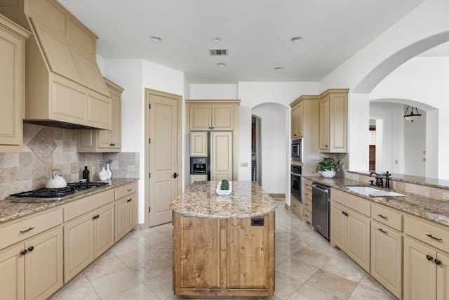 219 Jack Nicklaus Dr, Austin, TX 78738 - kitchen with cream cabinetry, built in appliances, a kitchen island, decorative backsplash, and light stone counters
