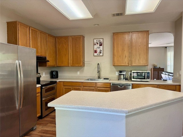 2201 Ezra Ct, Cedar Park, TX 78613 - kitchen with stainless steel appliances, a sink, arched walkways, under cabinet range hood, and dark wood-type flooring