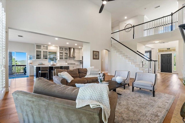 living area featuring arched walkways, stairway, a high ceiling, light wood-style flooring, and ceiling fan