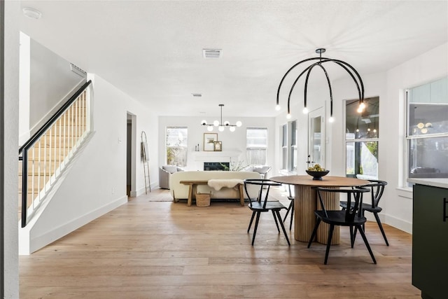 dining space featuring light wood finished floors, a chandelier, stairway, and a healthy amount of sunlight