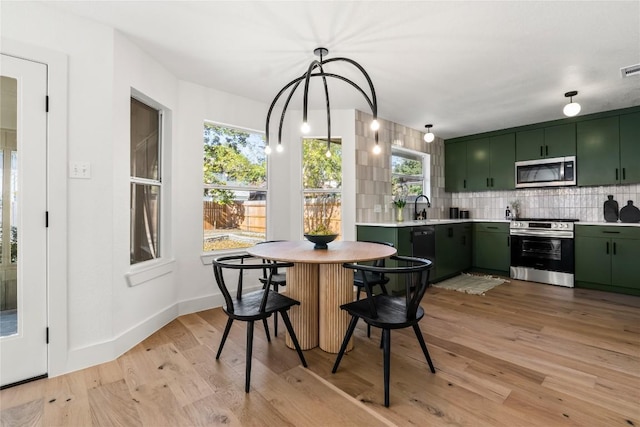 kitchen featuring light wood-style floors, green cabinets, light countertops, stainless steel appliances, and backsplash