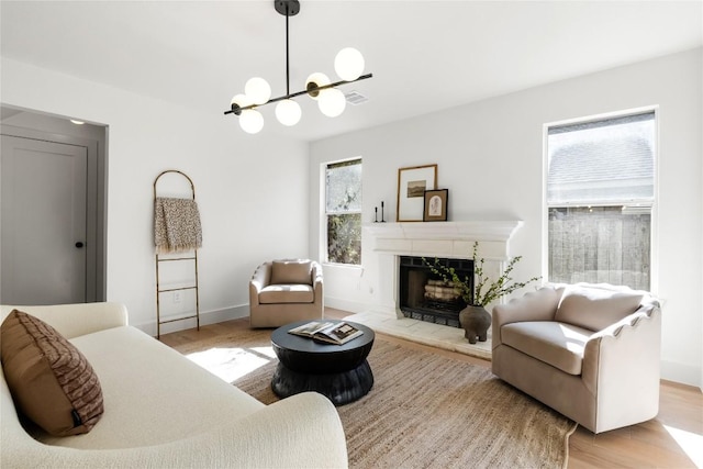 living area with a chandelier, a tile fireplace, light wood-type flooring, and baseboards