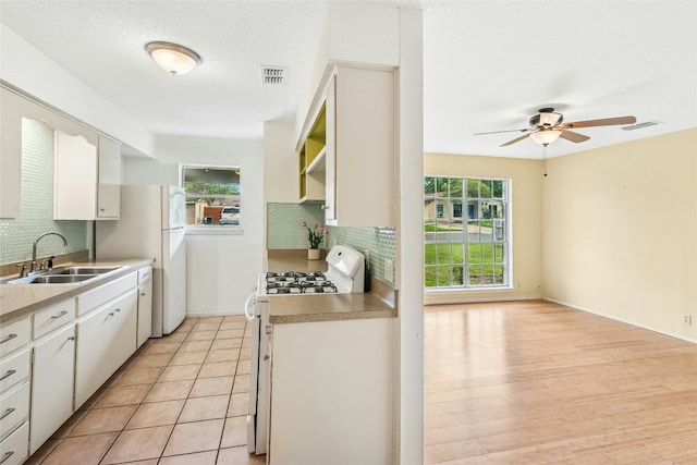 kitchen featuring visible vents, a sink, white appliances, decorative backsplash, and ceiling fan