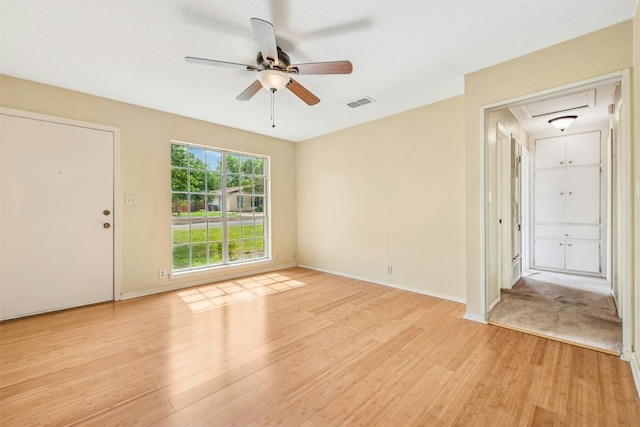 unfurnished room with attic access, light wood-style floors, visible vents, and ceiling fan