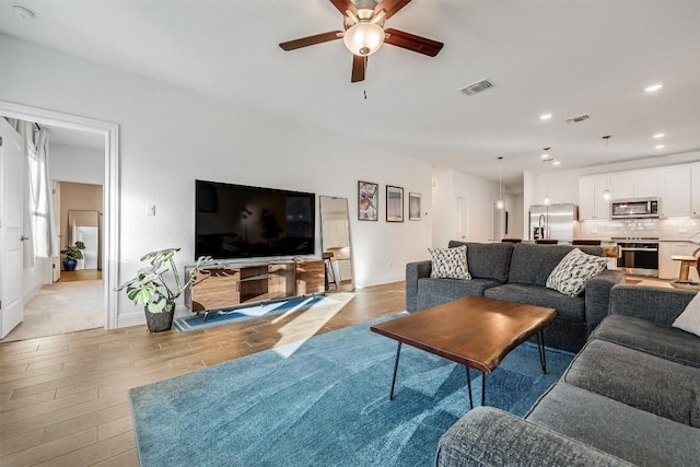 living room with visible vents, light wood-type flooring, baseboards, and ceiling fan
