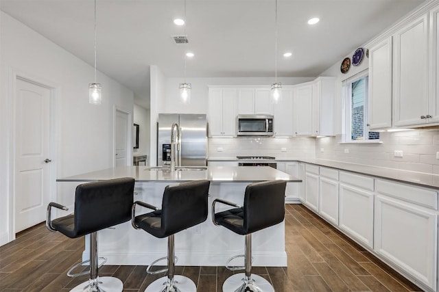 kitchen with dark wood-type flooring, visible vents, a breakfast bar area, decorative backsplash, and appliances with stainless steel finishes
