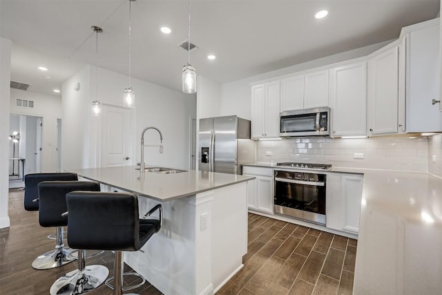 kitchen featuring visible vents, a sink, dark wood finished floors, a center island with sink, and stainless steel appliances