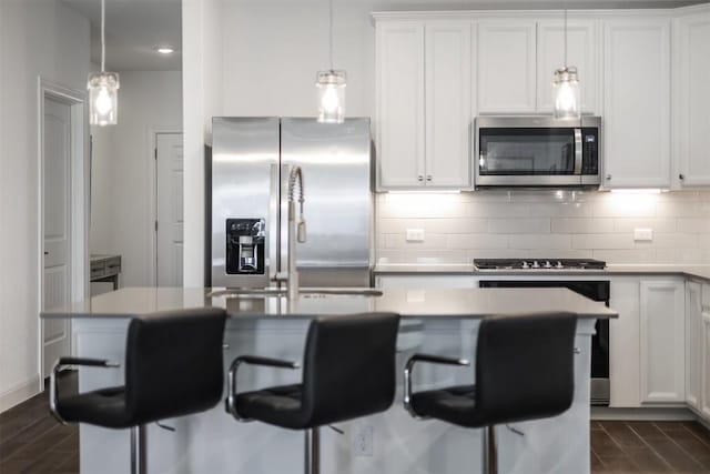 kitchen featuring white cabinetry, a center island with sink, decorative backsplash, appliances with stainless steel finishes, and hanging light fixtures