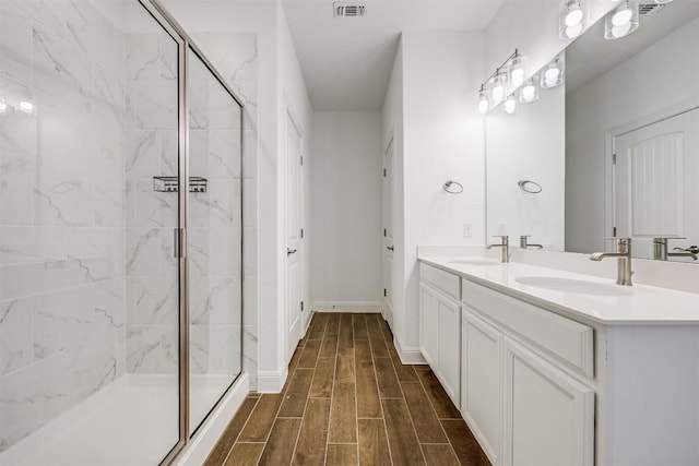 full bath featuring double vanity, a sink, a marble finish shower, and wood finished floors