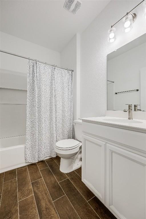 full bathroom with shower / tub combo, vanity, wood finish floors, toilet, and visible vents