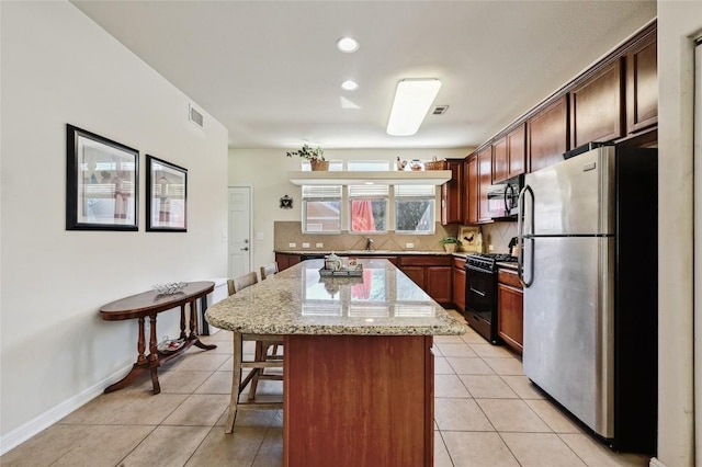 189 Grace, Kyle, TX 78640 - kitchen featuring black appliances, a kitchen breakfast bar, a center island, light tile patterned floors, and light stone counters