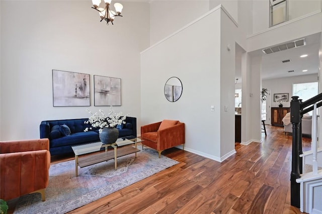 living area featuring a notable chandelier, visible vents, a high ceiling, and wood finished floors