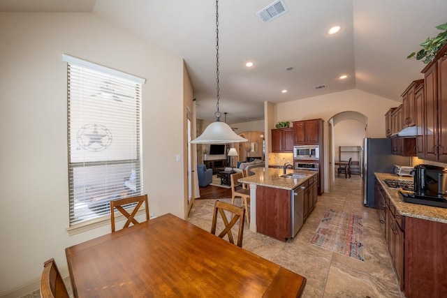 kitchen featuring arched walkways, vaulted ceiling, a sink, stainless steel appliances, and an island with sink
