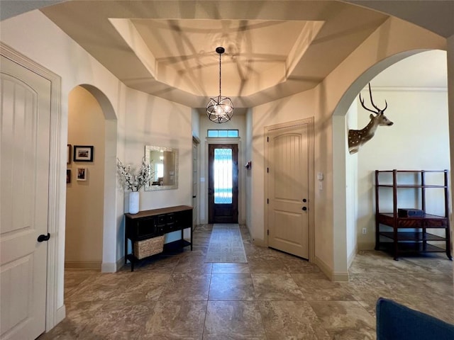 foyer entrance featuring arched walkways, a tray ceiling, a chandelier, and baseboards