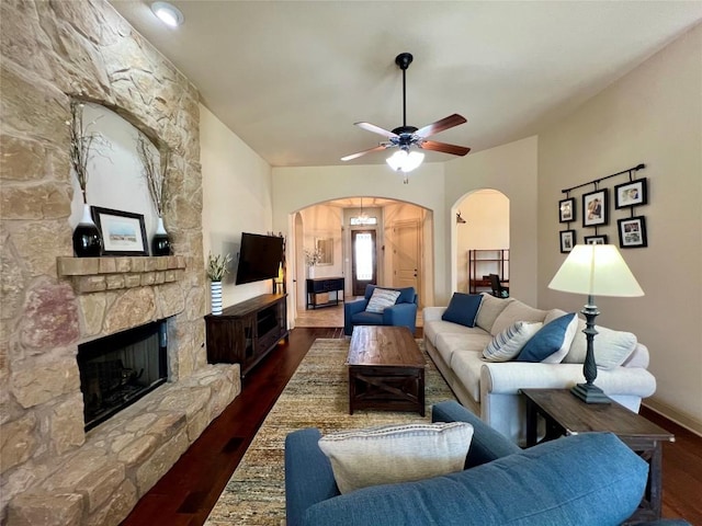 living room featuring a ceiling fan, arched walkways, a fireplace, wood finished floors, and baseboards