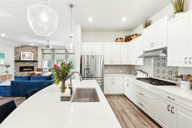 128 Mountain Lion Rd, Georgetown, TX 78628 - kitchen with appliances with stainless steel finishes, under cabinet range hood, light countertops, tasteful backsplash, and light wood-style flooring