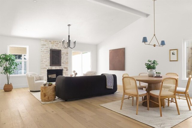 dining space featuring a chandelier, beam ceiling, light wood-style flooring, healthy amount of natural light, and a large fireplace