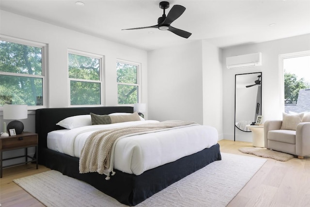 bedroom featuring a wall unit AC, multiple windows, wood finished floors, and ceiling fan