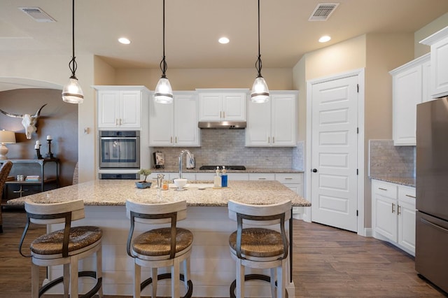 109 Grand Oaks Ln, Georgetown, TX 78628 - kitchen featuring stainless steel appliances, under cabinet range hood, dark wood-style floors, white cabinetry, and backsplash