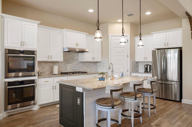 109 Grand Oaks Ln, Georgetown, TX 78628 - kitchen with stainless steel appliances, wood finished floors, backsplash, a kitchen island with sink, and white cabinetry