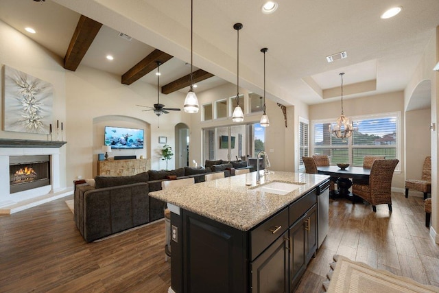 109 Grand Oaks Ln, Georgetown, TX 78628 - kitchen featuring a warm lit fireplace, dark wood finished floors, light stone countertops, a ceiling fan, and beam ceiling