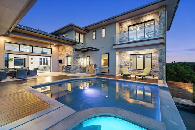 back of property at dusk with stone siding, area for grilling, a balcony, and an outdoor living space