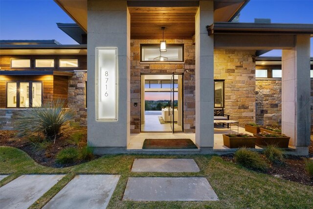 view of exterior entry with stone siding, covered porch, and stucco siding