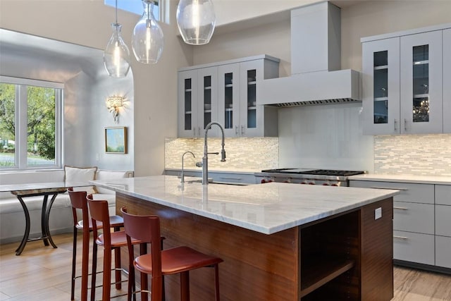 kitchen featuring an island with sink, wine cooler, wall chimney range hood, gray cabinets, and a sink