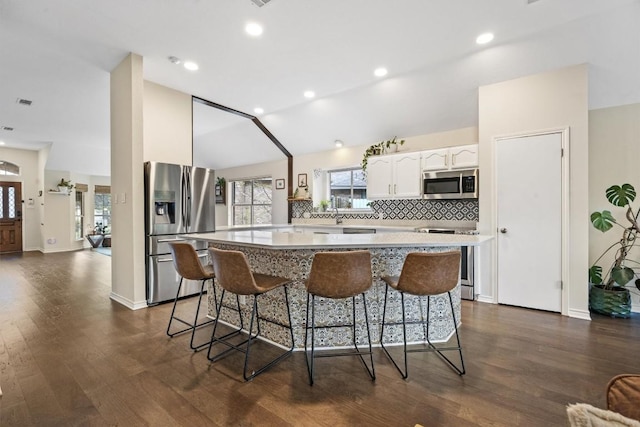 7306 Holly Fern Cv, Austin, TX 78750 - kitchen with stainless steel appliances, a center island, white cabinets, a kitchen breakfast bar, and backsplash
