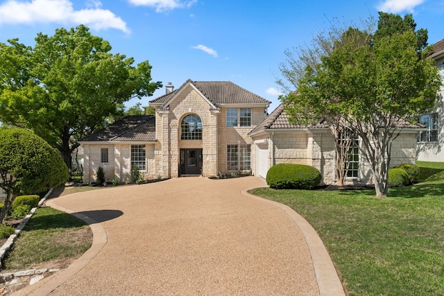 6 Dovedale Cv, The Hills, TX 78738 - traditional-style home featuring stone siding, a garage, concrete driveway, a chimney, and a front lawn