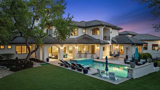 back of property at dusk featuring a yard, an outdoor hangout area, a patio area, and stucco siding