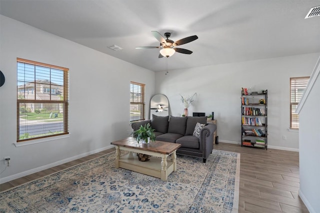 living area with baseboards, a ceiling fan, wood finished floors, and visible vents