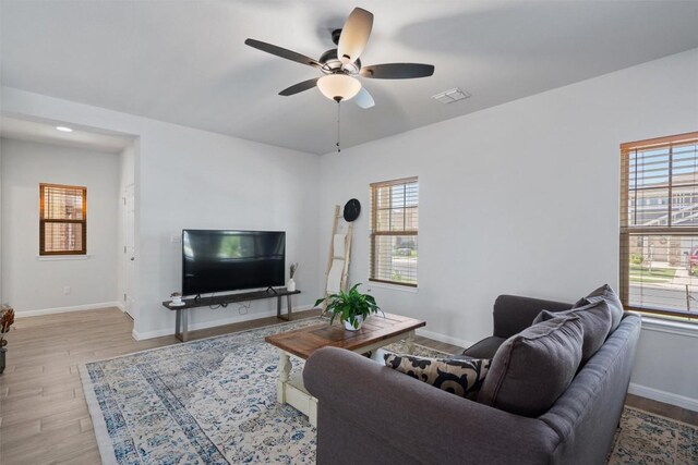 living room with a ceiling fan, baseboards, visible vents, and light wood finished floors