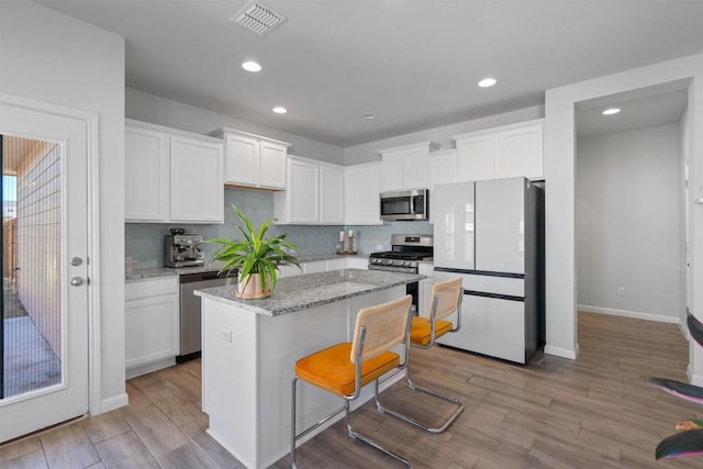 kitchen with appliances with stainless steel finishes, a center island, wood finished floors, white cabinets, and recessed lighting