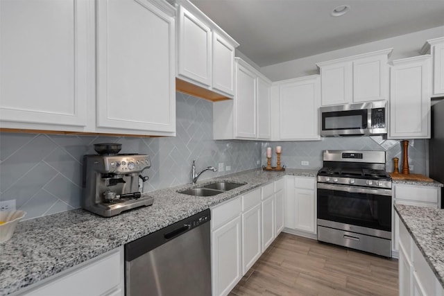 kitchen with white cabinets, tasteful backsplash, light stone counters, a sink, and appliances with stainless steel finishes
