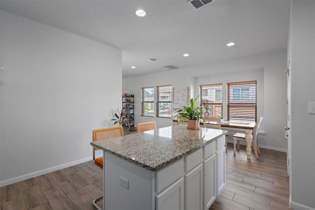 kitchen with visible vents, a center island, wood finished floors, baseboards, and white cabinetry