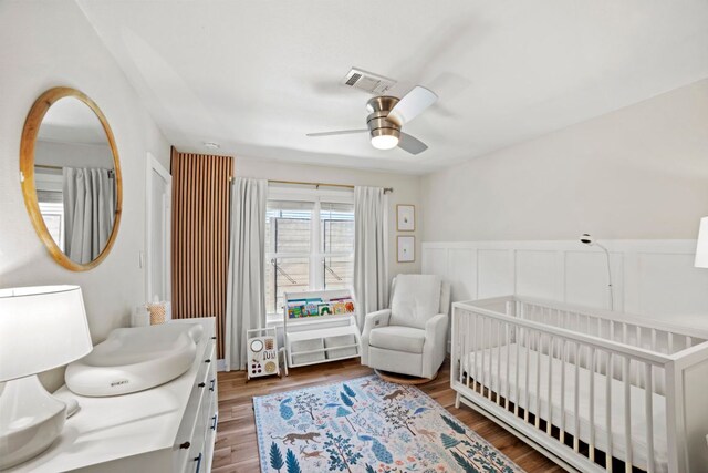 6009 Grover Ave, Austin, TX 78757 - bedroom with a crib, a wainscoted wall, wood finished floors, and a ceiling fan