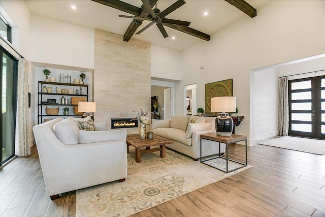 518 Doe Whisper Way, Austin, TX 78738 - living room featuring a high ceiling, beamed ceiling, a tile fireplace, ceiling fan, and light wood-type flooring