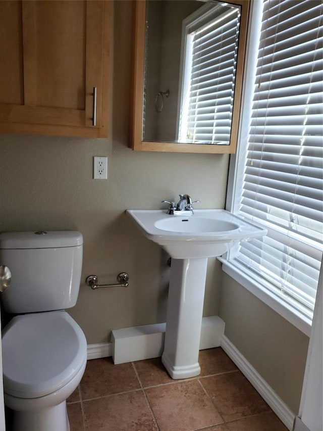 half bathroom with tile patterned floors, toilet, plenty of natural light, and baseboards