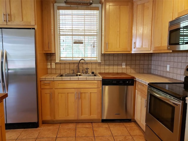 kitchen featuring light brown cabinetry, appliances with stainless steel finishes, a sink, and tile countertops