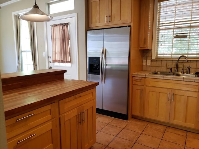 kitchen with butcher block counters, stainless steel refrigerator with ice dispenser, light tile patterned flooring, a sink, and backsplash