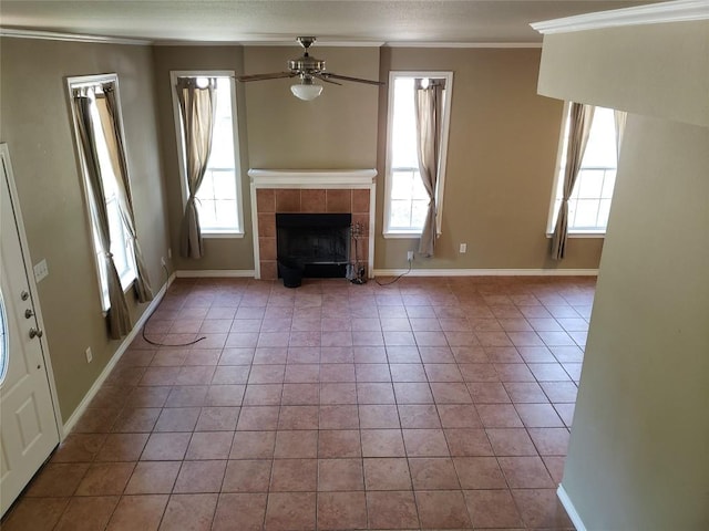 unfurnished living room featuring ornamental molding, a ceiling fan, a tiled fireplace, tile patterned floors, and baseboards