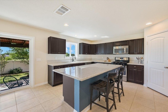 11208 Mickelson Dr, Austin, TX 78747 - kitchen featuring appliances with stainless steel finishes, light tile patterned floors, a breakfast bar, dark brown cabinetry, and a center island