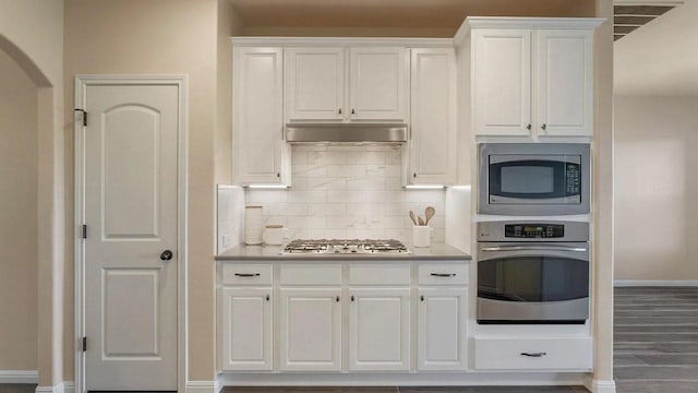 12325 Labrador Bay Ct, Austin, TX 78732 - kitchen with stainless steel appliances, baseboards, under cabinet range hood, white cabinetry, and decorative backsplash