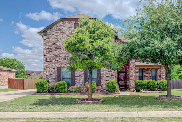 traditional-style home featuring brick siding, a front yard, and fence