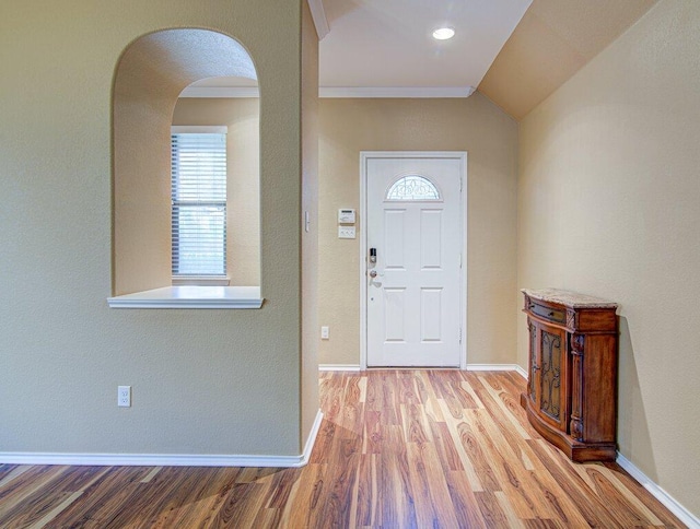 entryway with arched walkways, lofted ceiling, wood finished floors, and baseboards