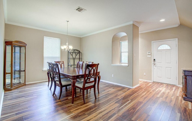 dining room with crown molding, wood finished floors, a chandelier, arched walkways, and baseboards